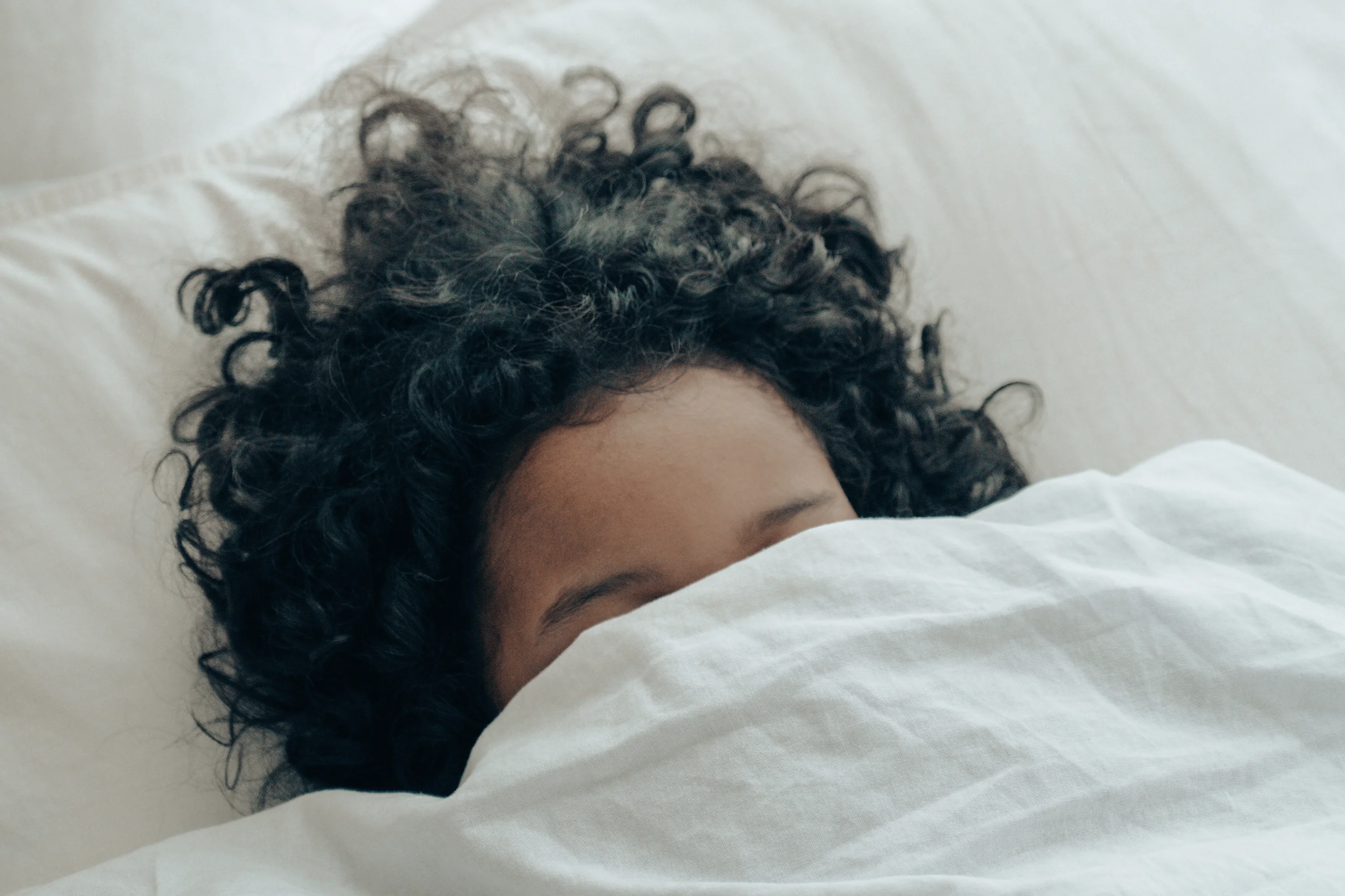 a person with their face under the covers in bed